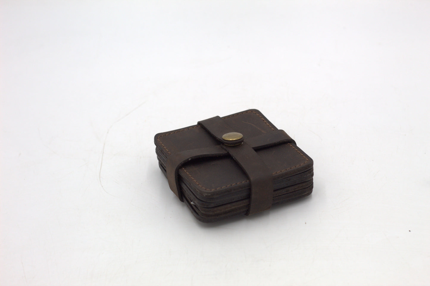 A set of four brown leather coasters with a holder.