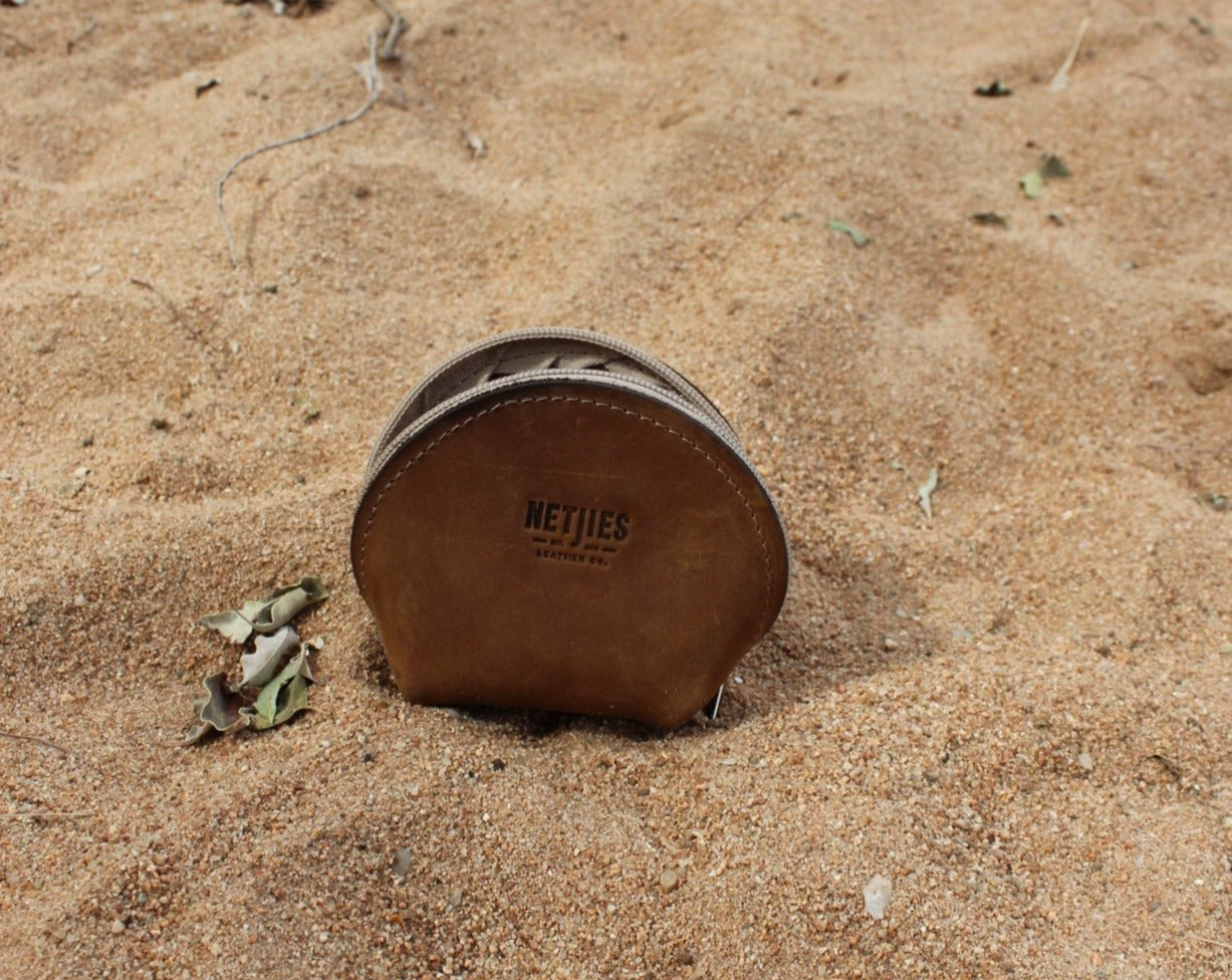 A brown leather coin purse lying on sandy ground with some small items scattered around it.