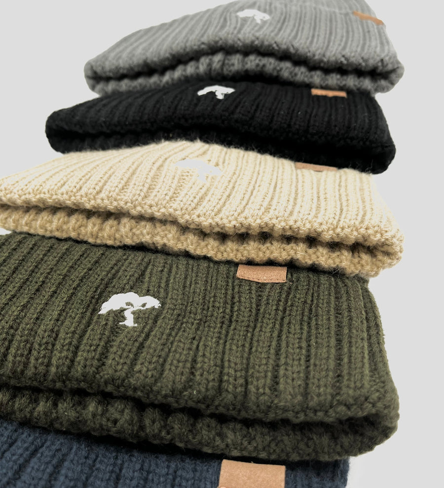 A stack of beanies in beige, black, and green colors, with a visible brand tag on all of them.