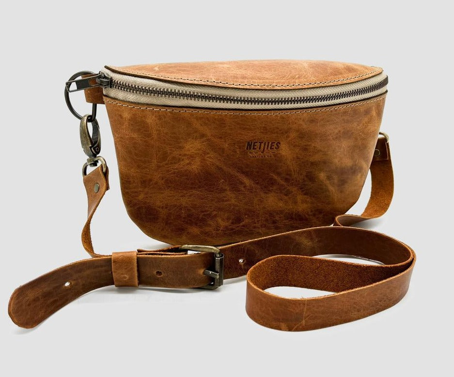 Brown leather crossbody bag with a zipper closure and a detachable strap, isolated on a white background.
