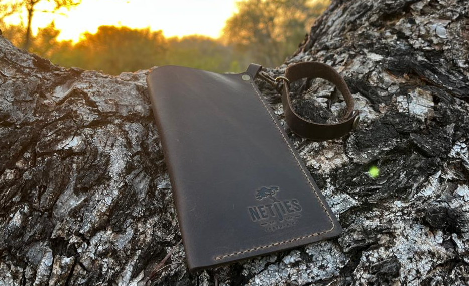 A black leather sunglasses carrier placed outside on a tree branch with a sunset background