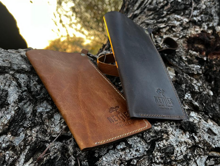 A brown leather sunglass carrier placed on a tree branch, with the logo "Netjies" visible on the bottom right side.