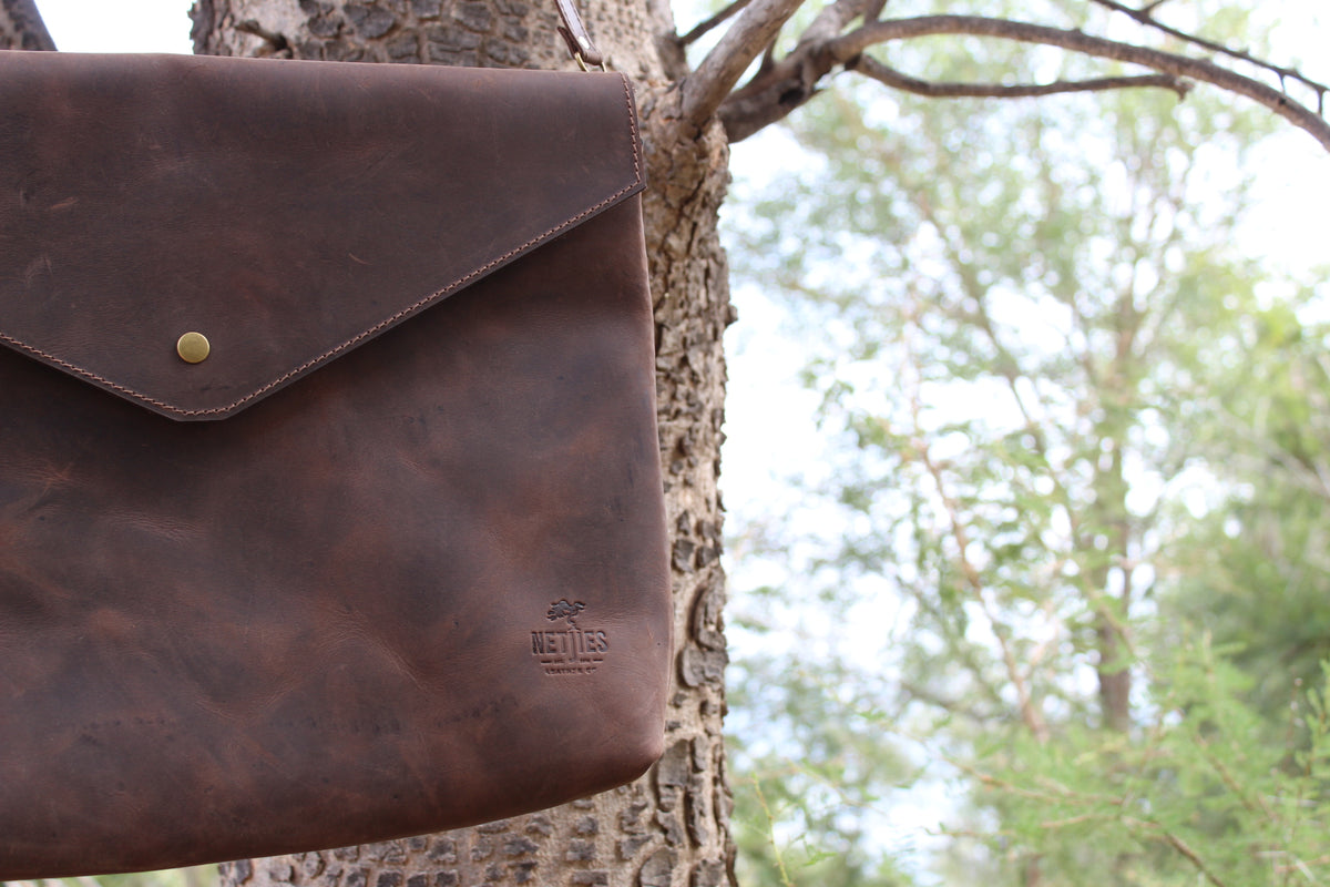 A brown leather laptop sling hanging from a tree branch.