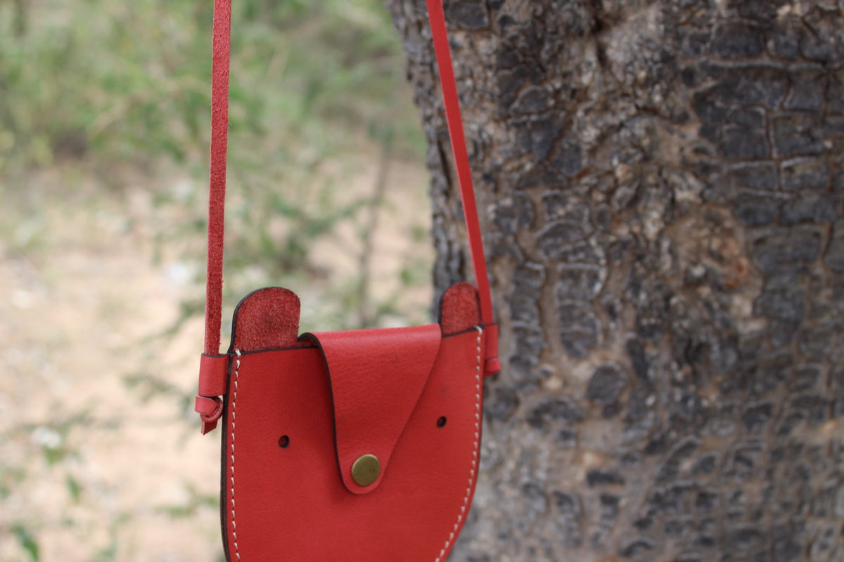 A red leather handbag with a flap closure and a metal snap button, displayed on a tree.