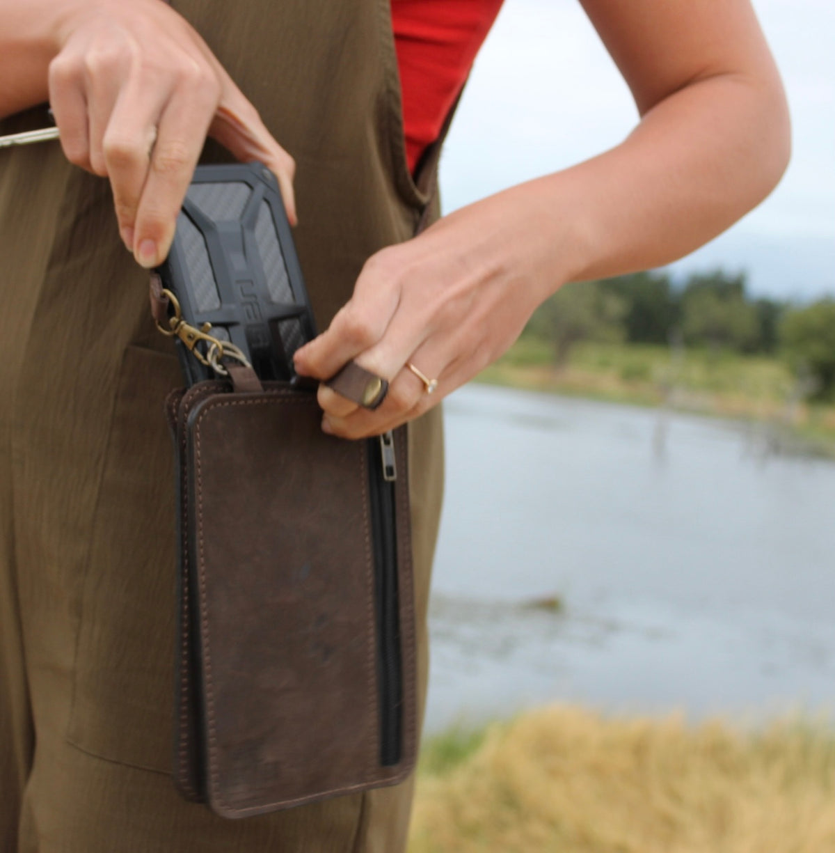 Person holding a brown leather bag with a blurred natural background