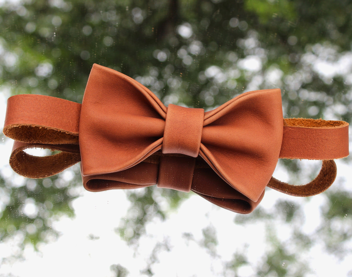 Brown leather bow tie placed on a mirror outdoors with a natural background