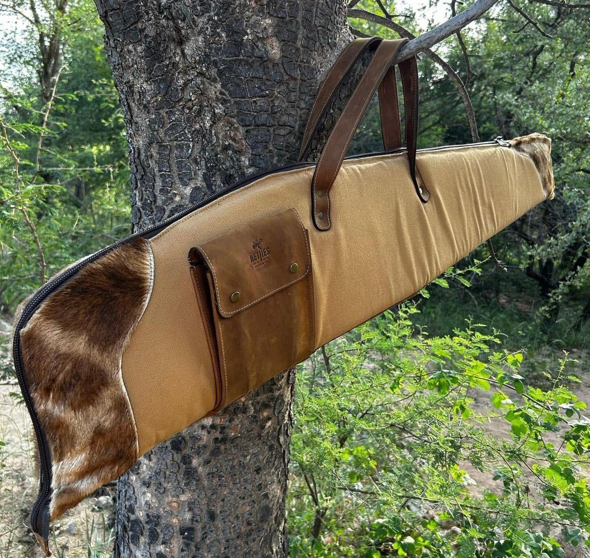A brown rifle bag with a leather strap and a section lined with animal fur, hanging on a tree outdoors.