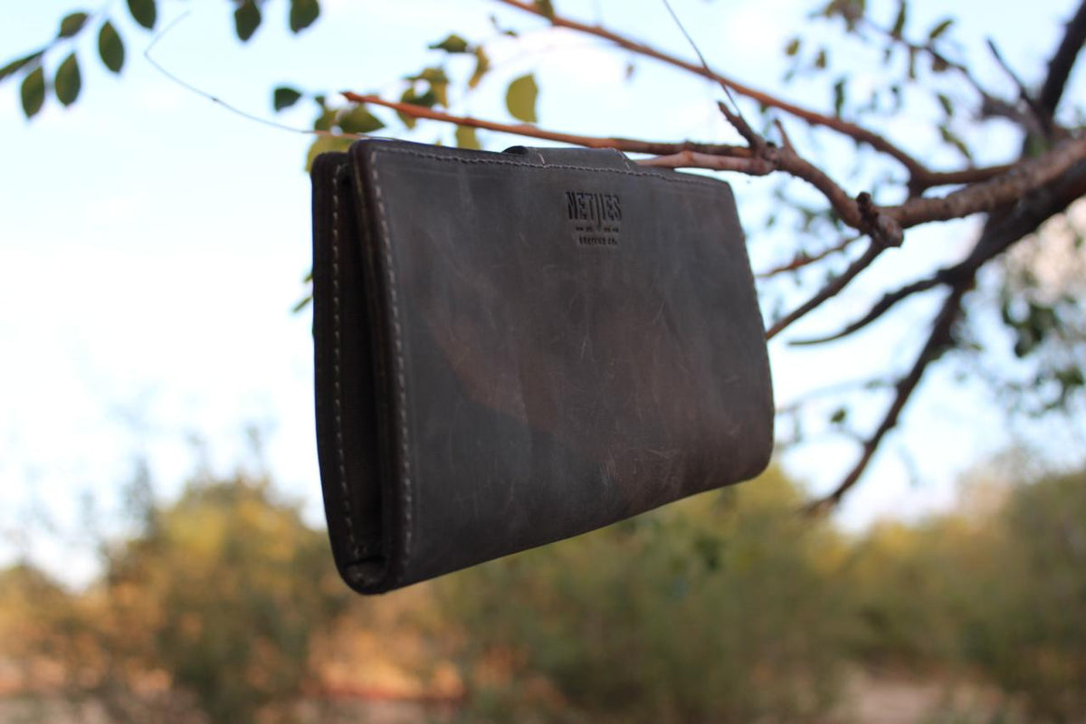 A black leather license holder hanging on a tree branch outdoors.