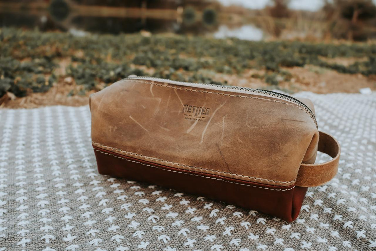 Brown leather toiletry bag on a textured surface with a blurred natural background