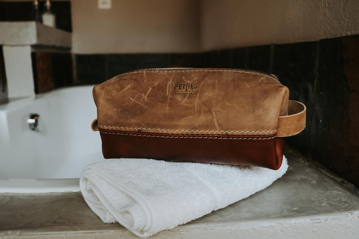 Brown leather toiletry bag on a white towel with a blurred bathroom background