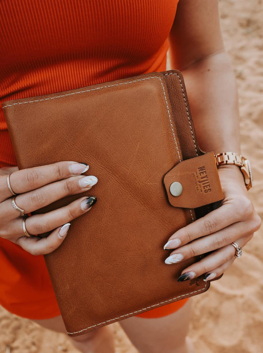 Person holding a brown leather notebook with a visible brand logo.