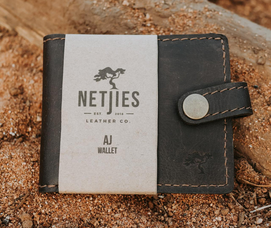 Black leather wallet with 'NETJIES' branding on a sandy background