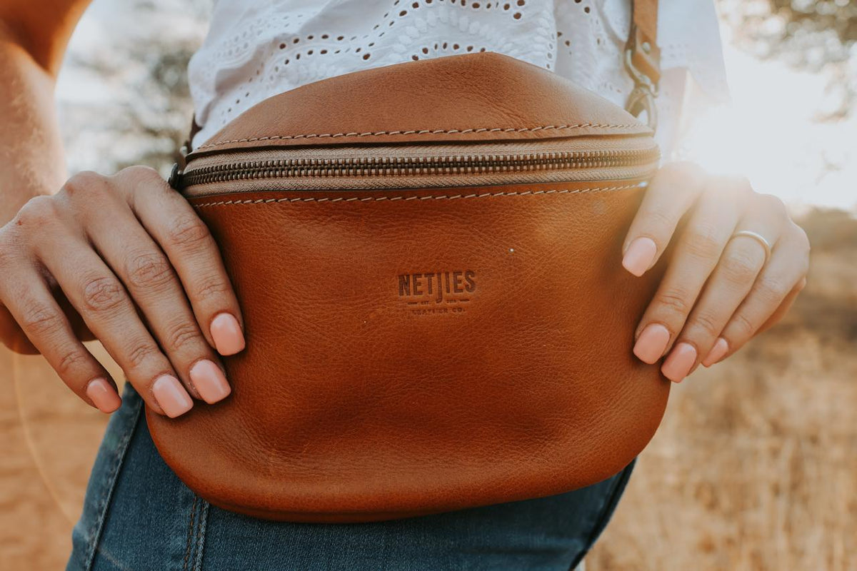 Brown leather bag with 'NETJIES' branding held by a person outdoors.