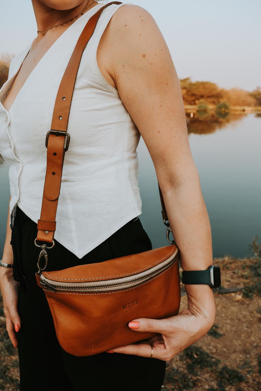 Person holding a brown leather bag with a blurred natural background