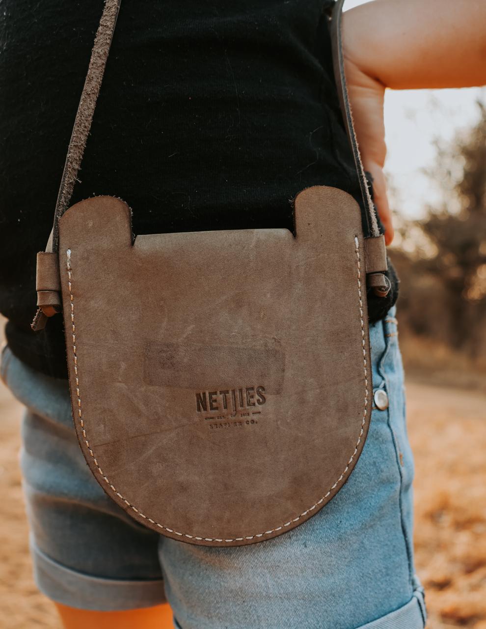 Brown leather bag with 'NETIES' branding held by a person outdoors.