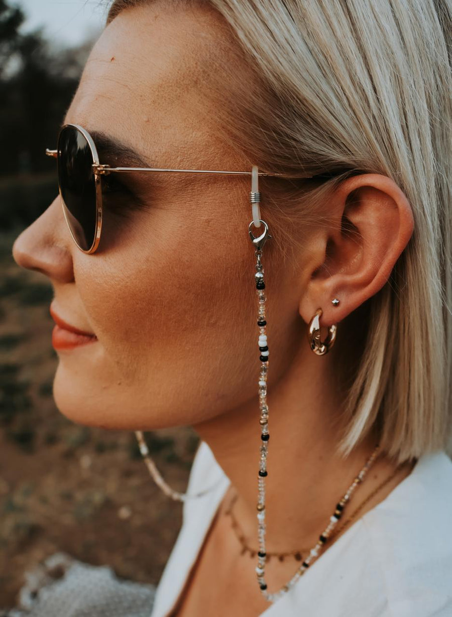 Close-up of a woman wearing sunglasses with a beaded toutjie, outdoors.