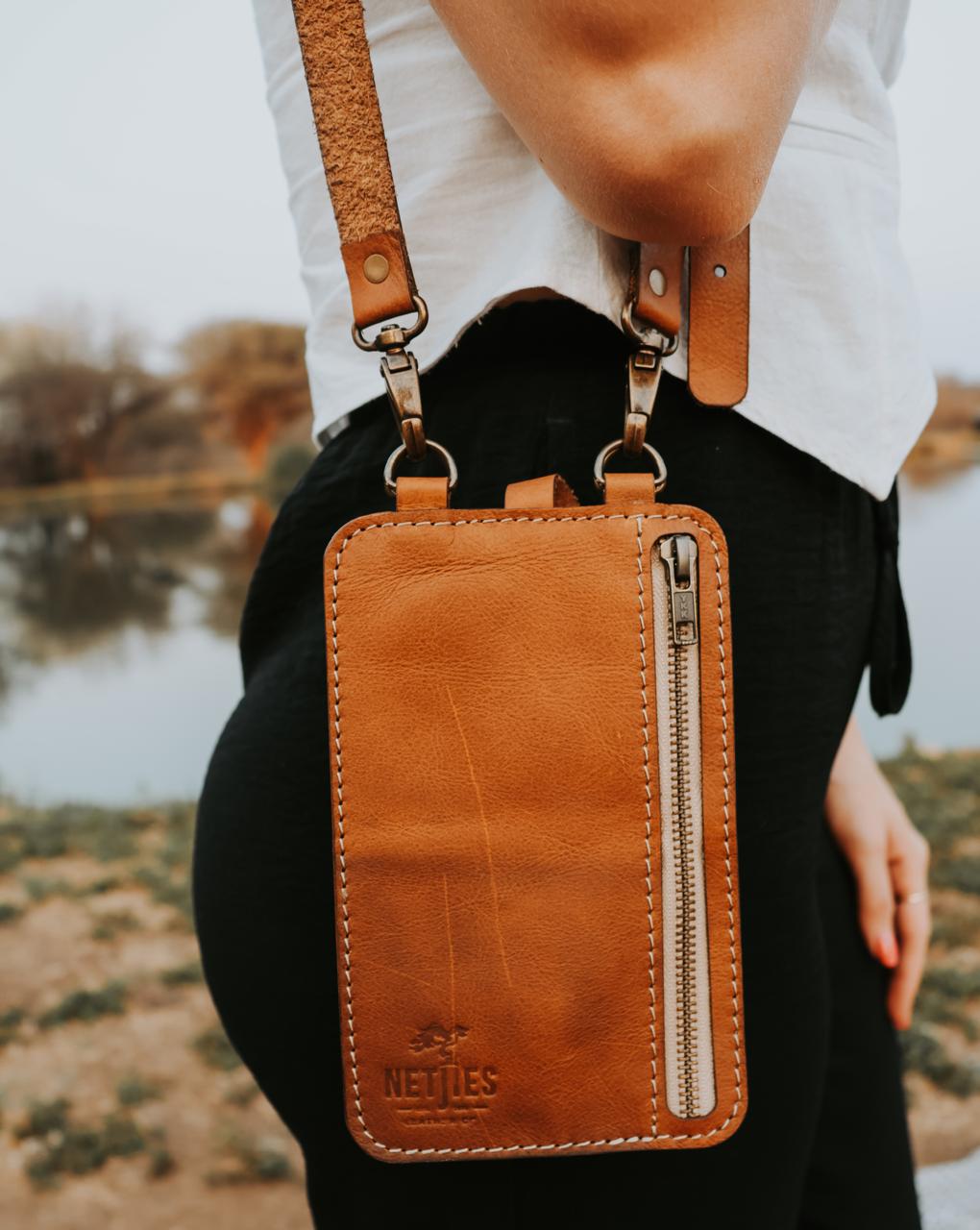 Brown leather crossbody bag with visible brand name held by a person outdoors.