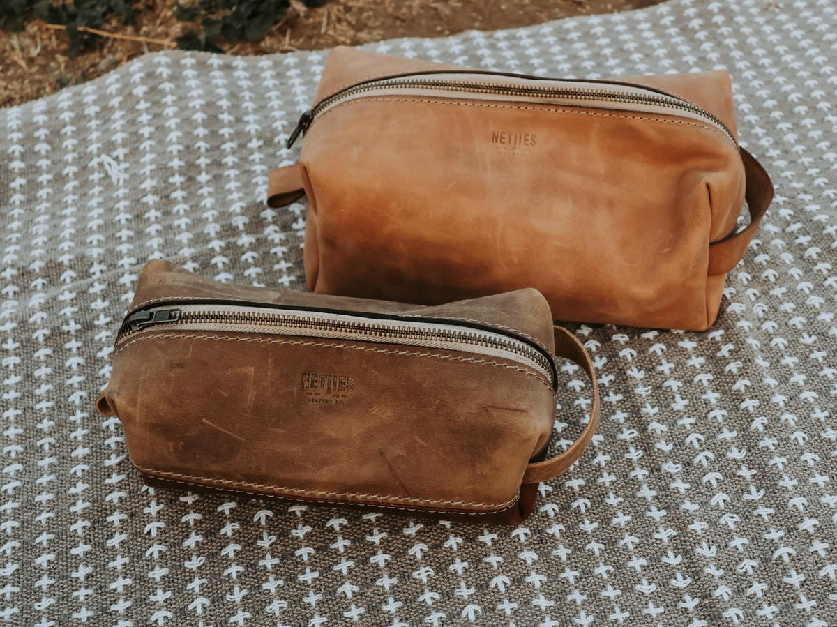 Two brown leather toiletry bags with 'NETJIES' branding on a textured fabric background.