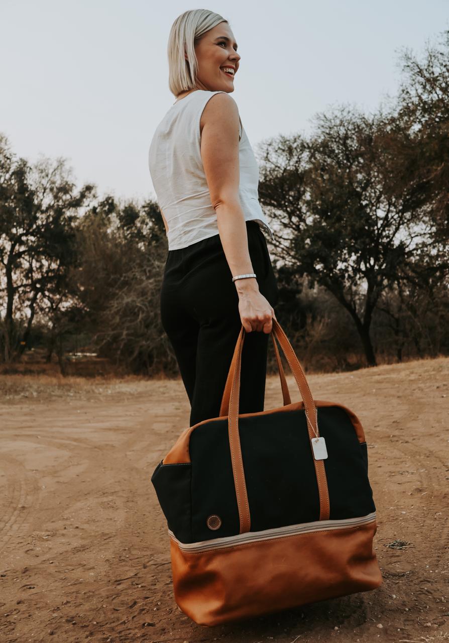 Woman holding a black and brown bag outdoors with trees in the background