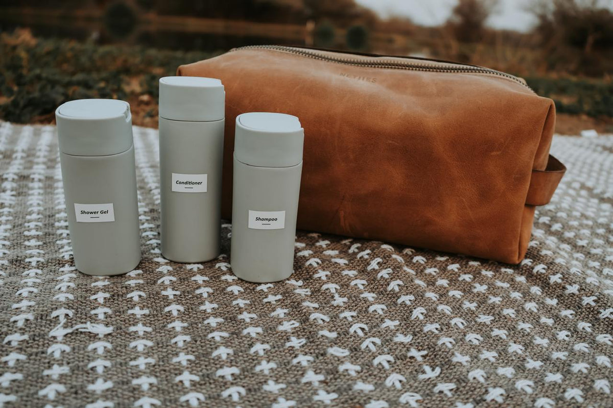 Three gray tumblers with labels next to a brown leather bag on a textured surface.