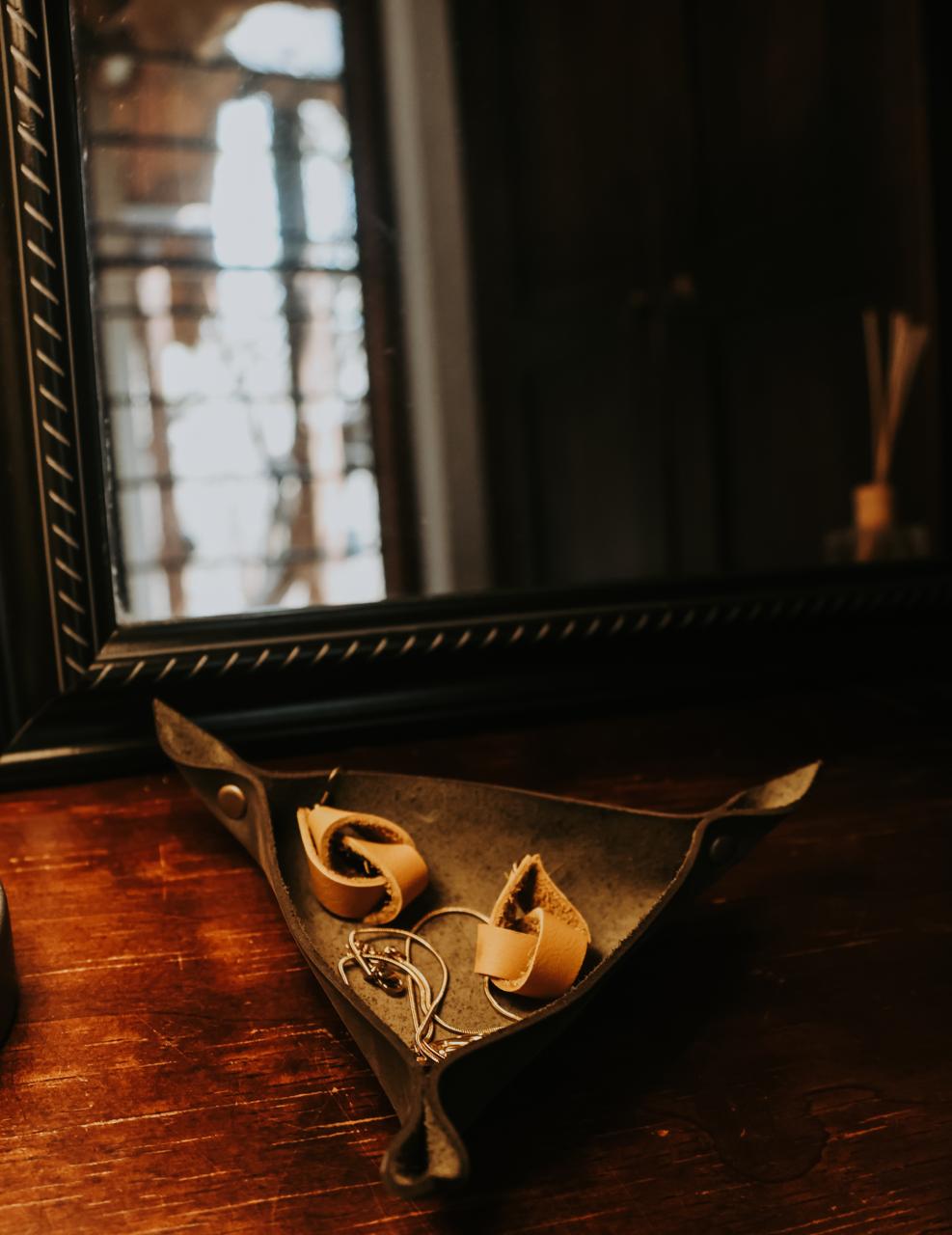 Pair of earrings in a brown leather jewelry holder on a dark wooden surface with a mirror in the background