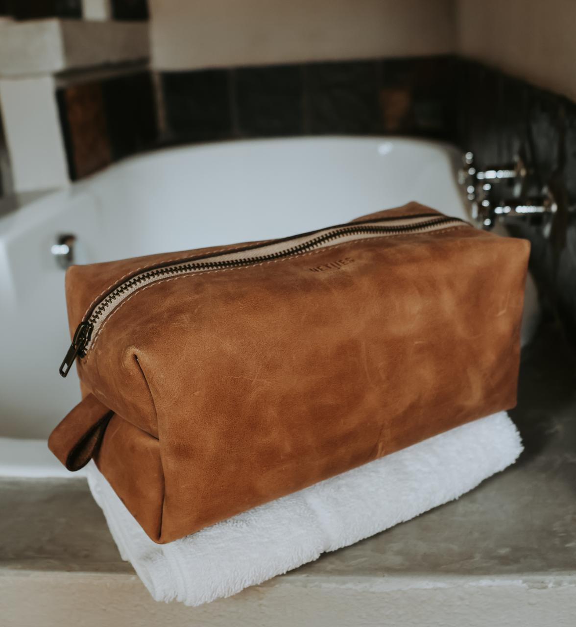 Brown leather toiletry bag on a white towel with a blurred bathroom background