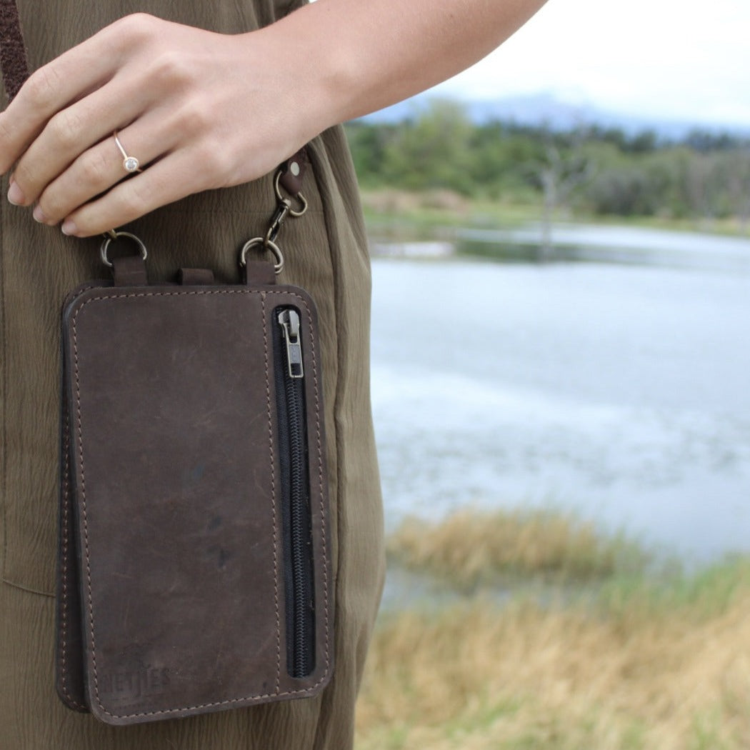 A person wearing a brown leather neck wallet while standing near a body of water.